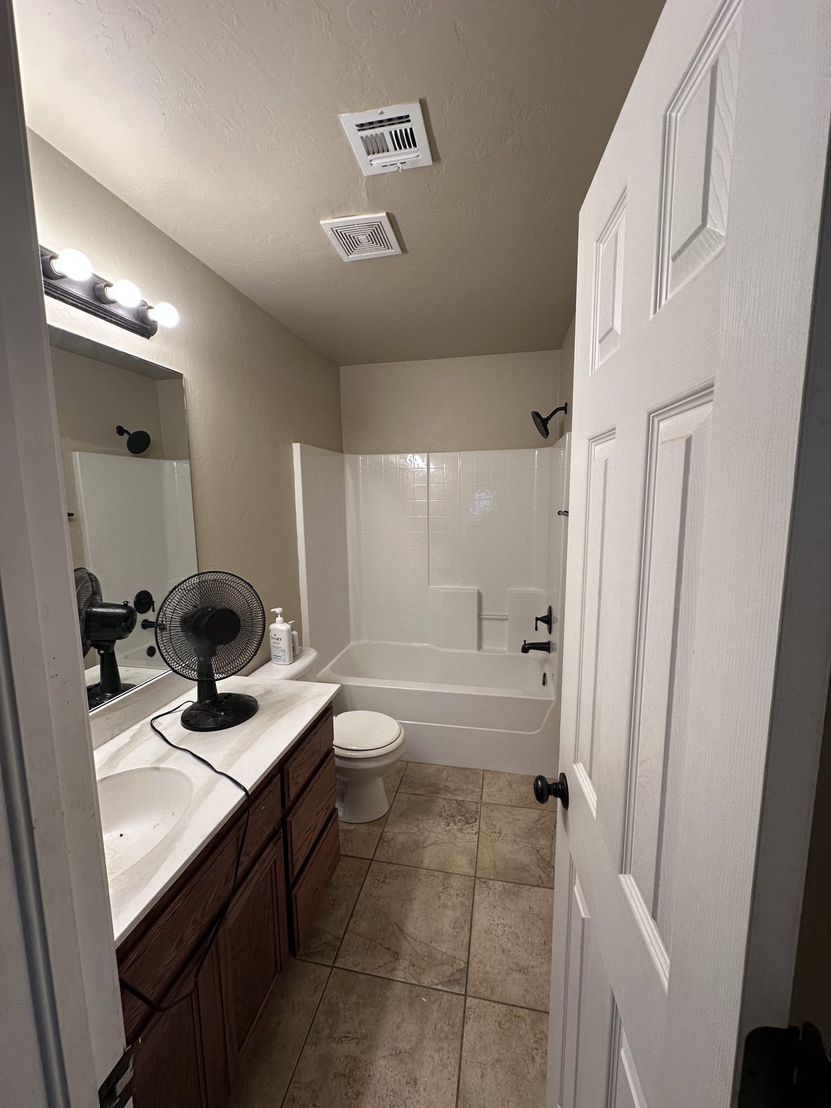 Finished bathroom remodel with a white tiled tub and shower surround, wood vanity, and new lighting