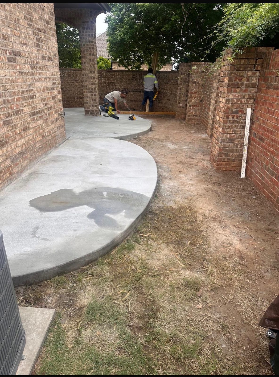 Curved concrete patio poured against a brick wall on an Oklahoma City metro home, with the crew still working in the background