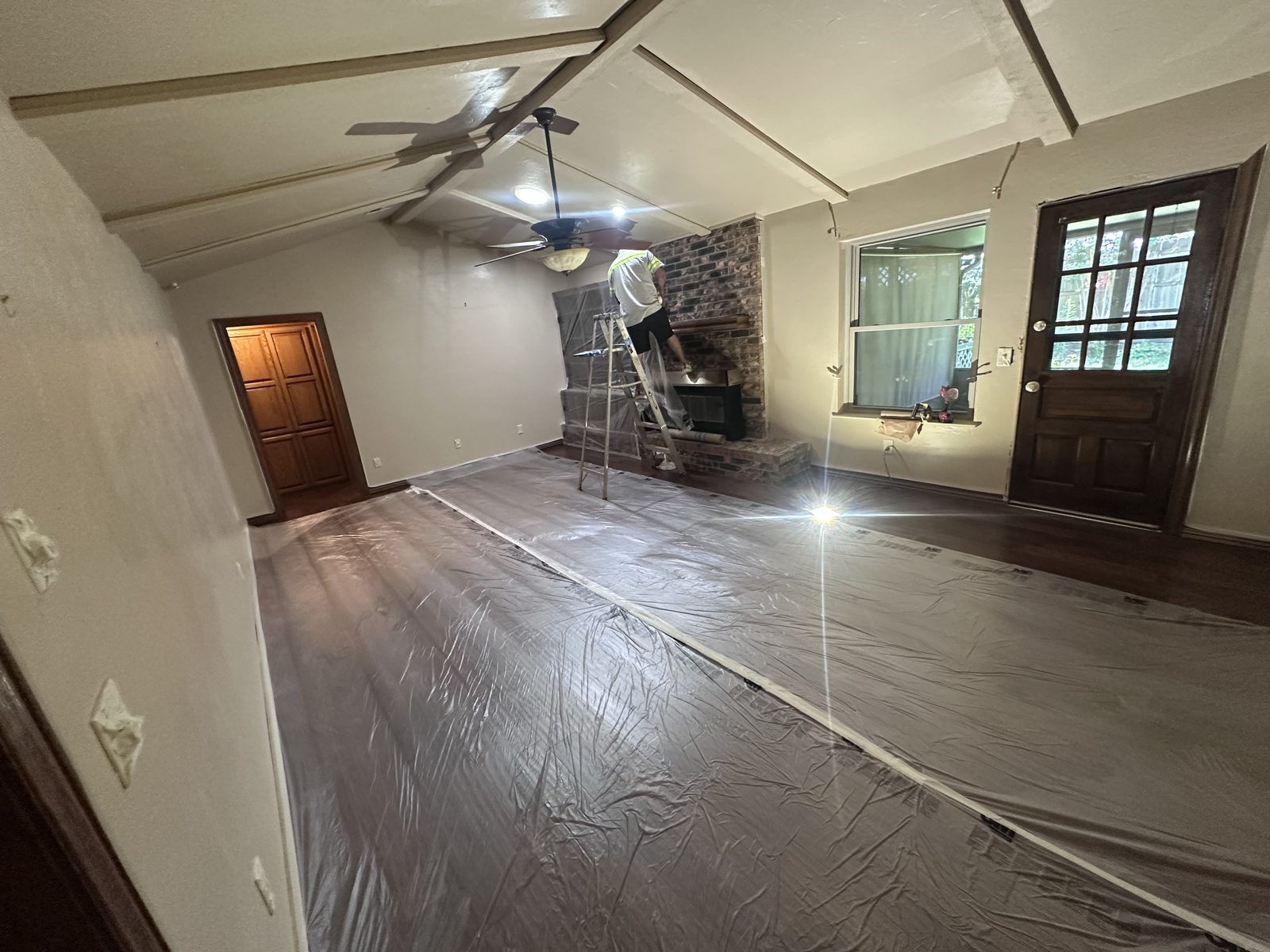 Interior room mid-remodel with fresh white walls and new hardwood flooring protected under sheeting